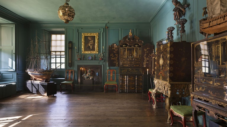 Interior shot of a panelled room, painted in a turquoise. Ornate display cabinets, built from dark woods and gold fixtures furnish the room, boldly contrasting with the colour of the walls.